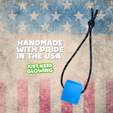 Blue, rechargeable glow in the dark cube with reflective paracord, handmade in the USA with pride. Emphasizes American manufacturing and visibility in low light. Just Keep Glowing. Perfect for camping, emergencies.