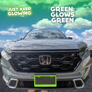 Green glow in the dark license plate frame illuminating the front of a black car, enhancing visibility and adding a unique style. Just Keep Glowing.