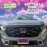 Glittery pink license plate frame emitting a vibrant purple glow, adding a unique and stylish touch to the front of a light-colored Honda CR-V. Just Keep Glowing.