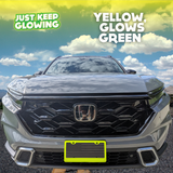 Yellow license plate frame emitting a vibrant green glow, adding a unique and stylish touch to the front of a light-colored Honda CR-V. Just Keep Glowing.