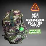 Camouflage backpack with a bright green glow in the dark cube attached, highlighting emergency preparedness and visibility in low light. Ideal for hiking, camping, and outdoor adventures. Just Keep Glowing.