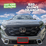 Red license plate frame emitting a vibrant orange glow, adding a unique and stylish touch to the front of a light-colored Honda CR-V. Just Keep Glowing.